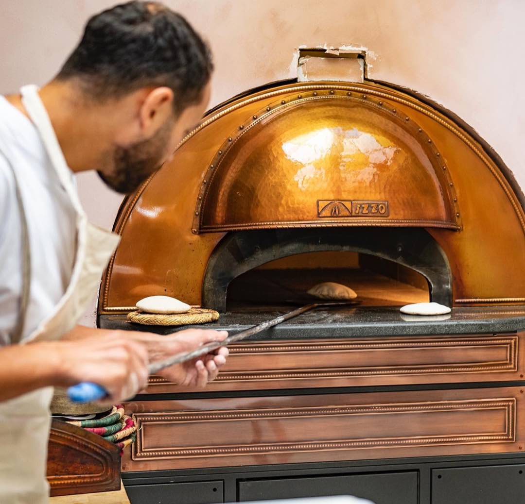 Baker sliding flatbread into the copper wood-fired oven